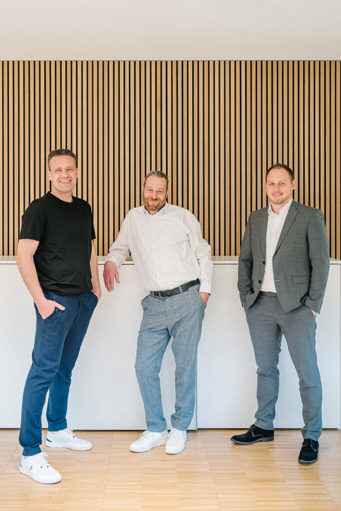Magnus Walk, Björn Stiefvater und Steffen Erbsland, die Geschäftsführer der Kanzlei Stiefvater & Walk, stehen locker vor einer Holzlamellenwand