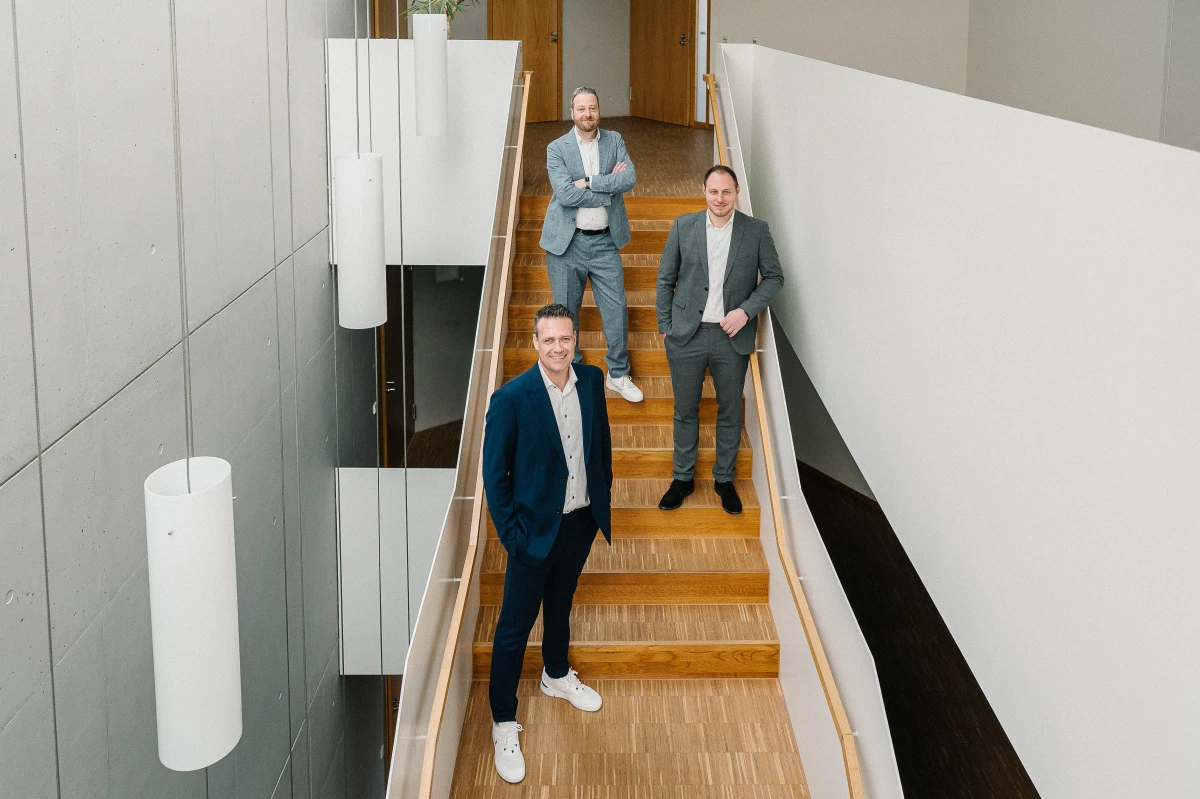 Die drei Geschäftsführer von Stiefvater & Walk – Magnus Walk, Björn Stiefvater und Steffen Erbsland – stehen versetzt auf einer modernen Holztreppe